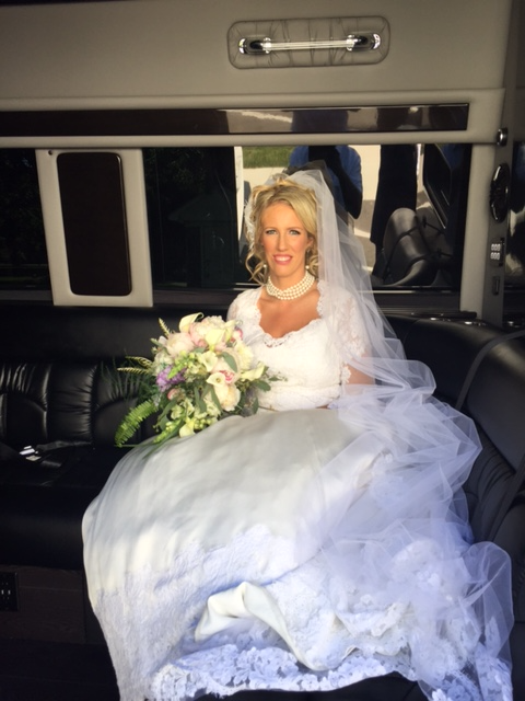 Bride seated inside stretch limousine holding wedding bouquet