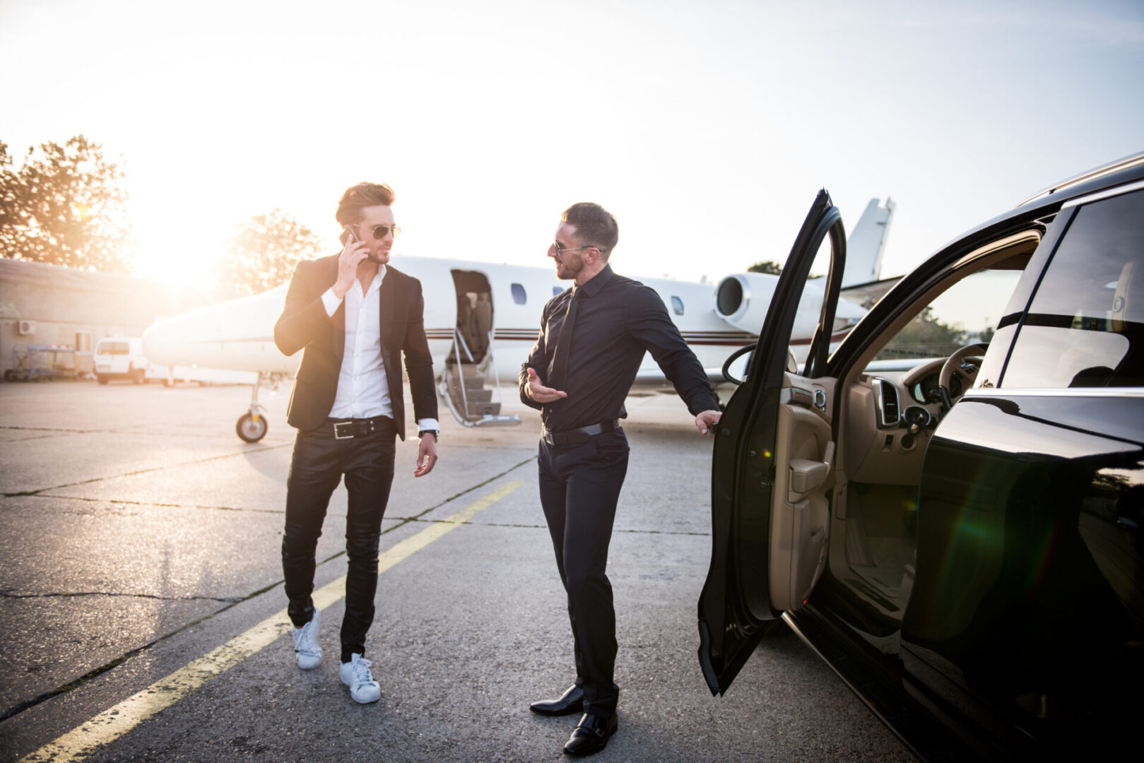 Two men standing next to a car and a plane.