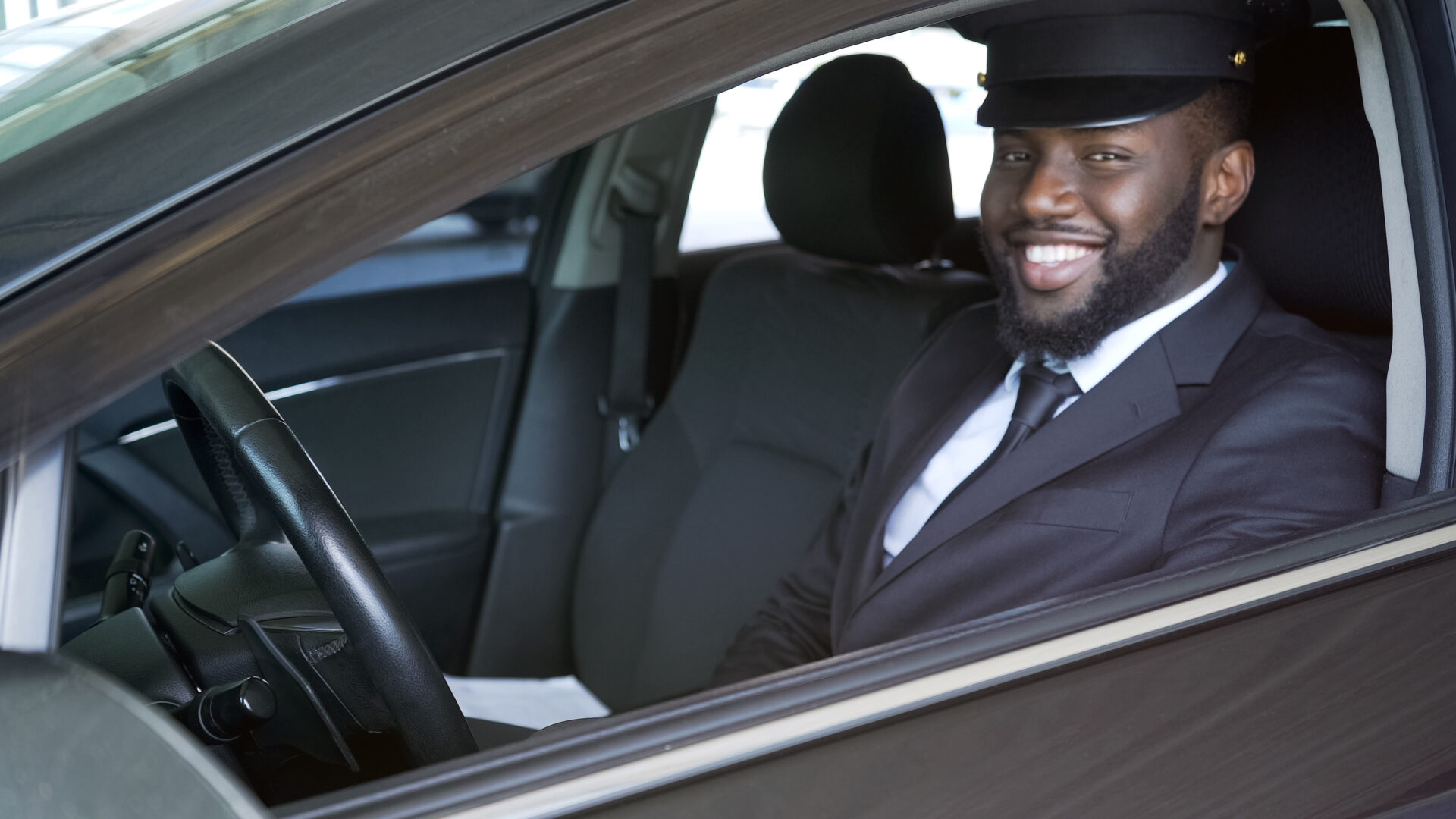 A man in a suit and hat sitting inside of a car.