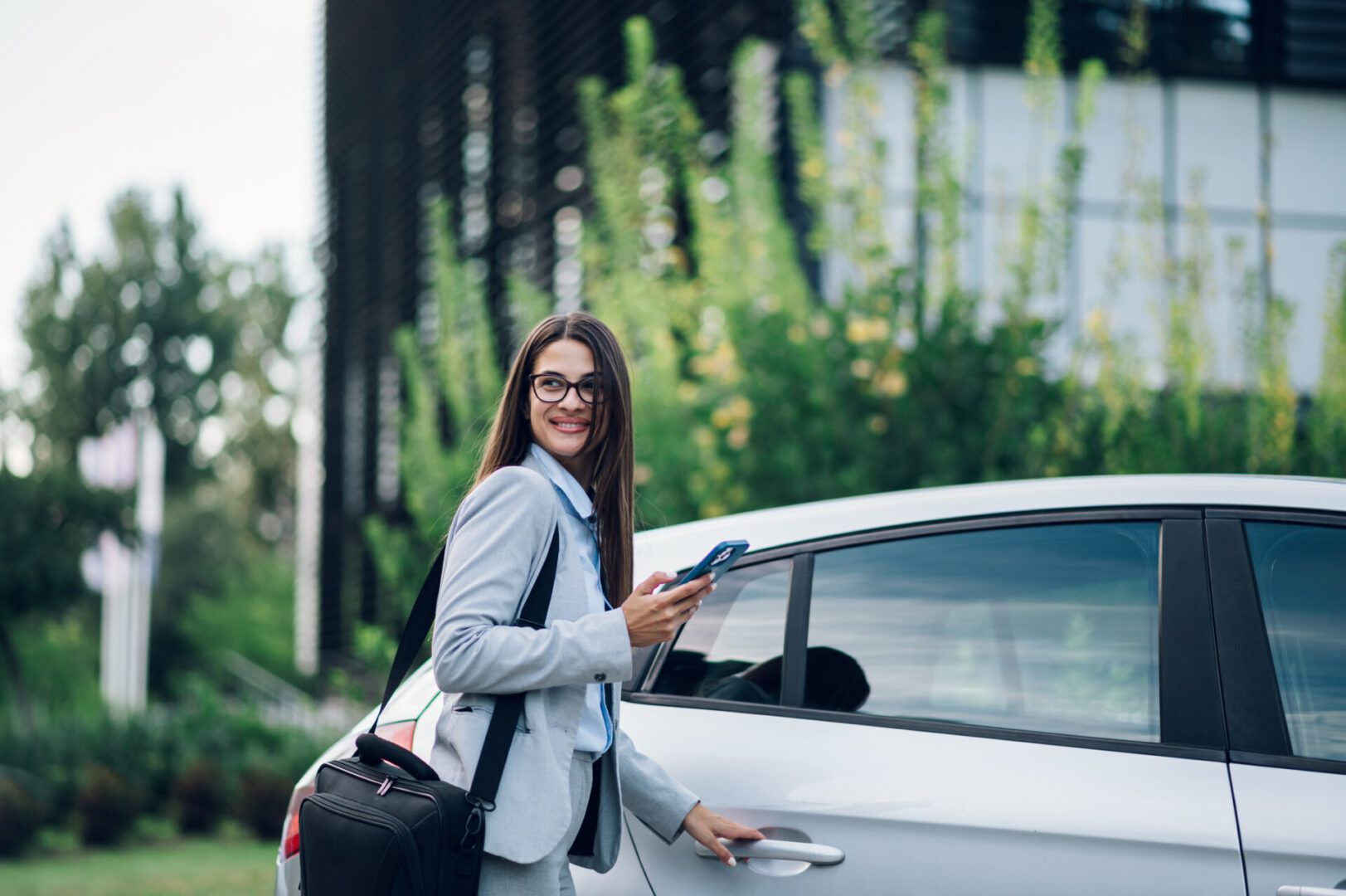 A woman standing next to her car holding a phone.